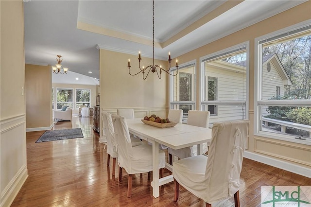 dining area with a raised ceiling, wood finished floors, an inviting chandelier, crown molding, and a decorative wall