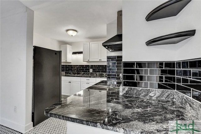 kitchen featuring backsplash, freestanding refrigerator, white cabinets, stovetop, and wall chimney exhaust hood