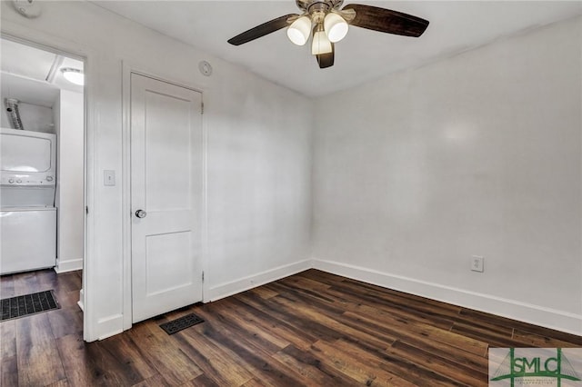 empty room featuring baseboards, dark wood-type flooring, and stacked washer and clothes dryer