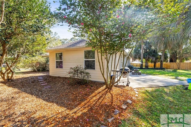 view of side of property with a patio, a yard, roof with shingles, and fence