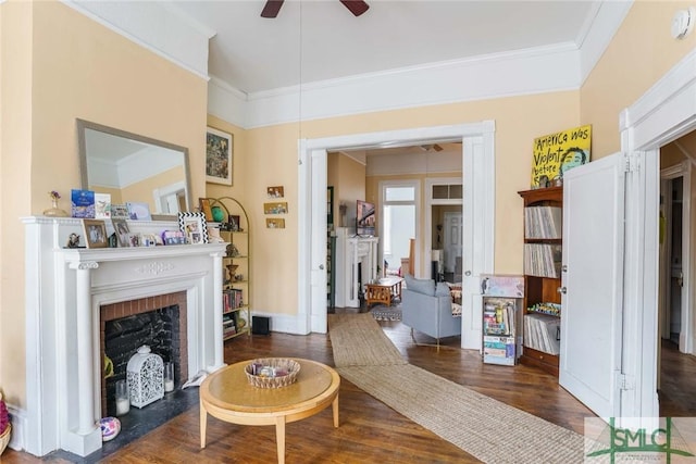 living area with ornamental molding, a ceiling fan, a fireplace, and wood finished floors