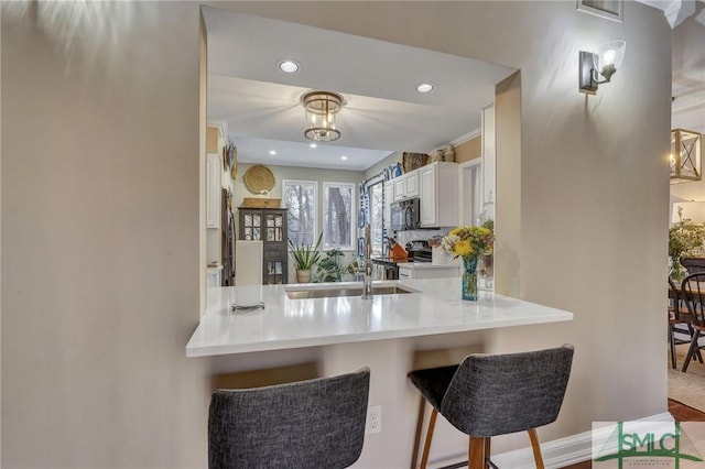 kitchen featuring stainless steel electric range, white cabinetry, black microwave, a peninsula, and a kitchen bar