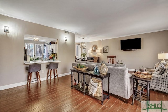 living room with wood finished floors, crown molding, baseboards, and an inviting chandelier