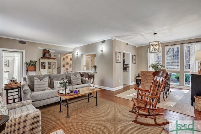 living room featuring wood finished floors, visible vents, baseboards, ornamental molding, and an inviting chandelier