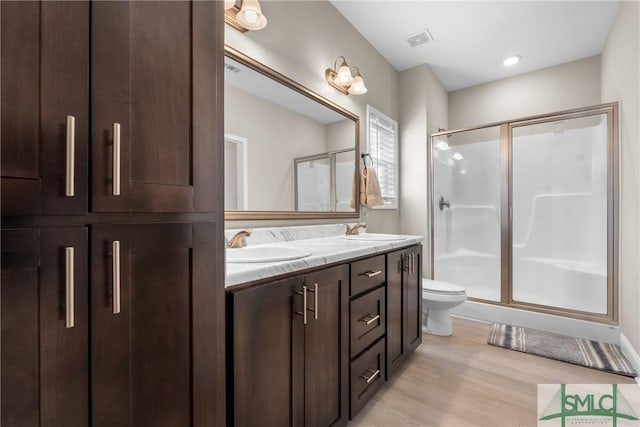 bathroom with double vanity, visible vents, a sink, a shower stall, and wood finished floors