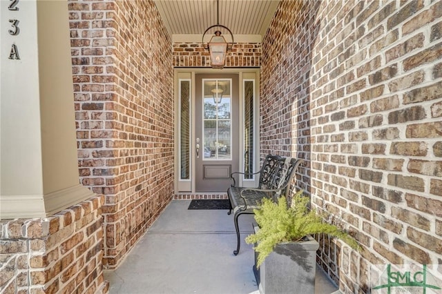 doorway to property featuring a porch and brick siding