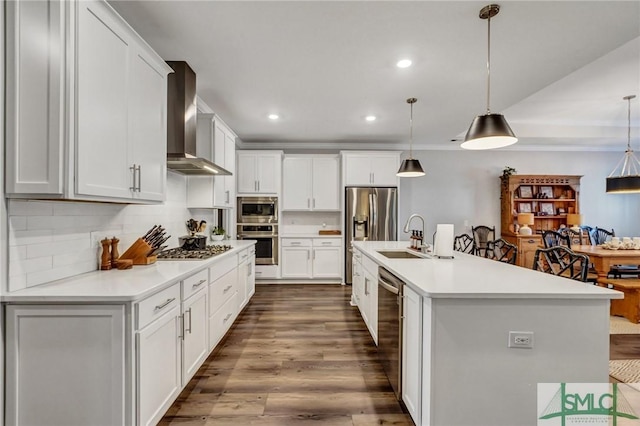 kitchen with stainless steel appliances, a sink, dark wood-style floors, wall chimney exhaust hood, and tasteful backsplash