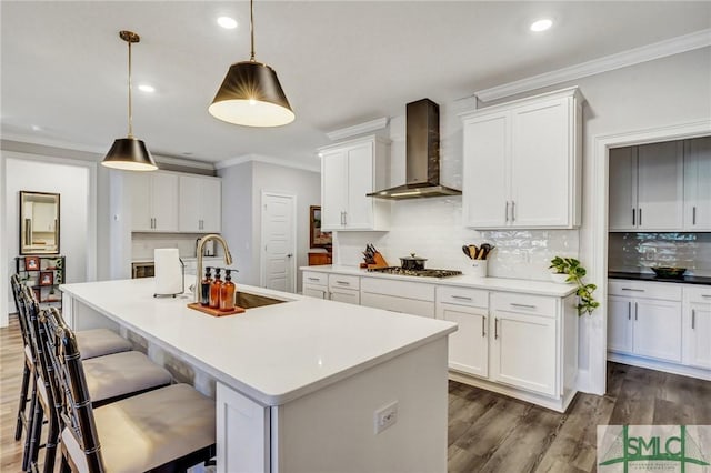 kitchen with stainless steel gas cooktop, dark wood-style flooring, a sink, wall chimney range hood, and crown molding