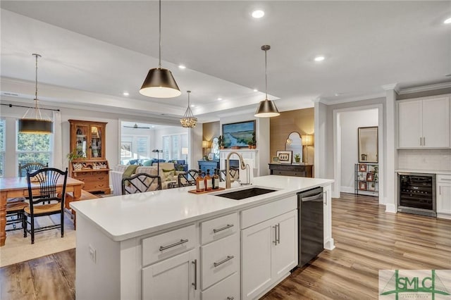 kitchen with beverage cooler, wood finished floors, a sink, stainless steel dishwasher, and a center island with sink