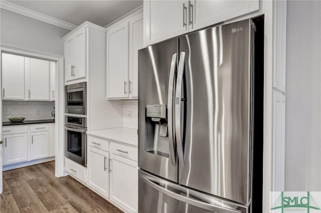 kitchen with stainless steel appliances, backsplash, ornamental molding, white cabinetry, and wood finished floors