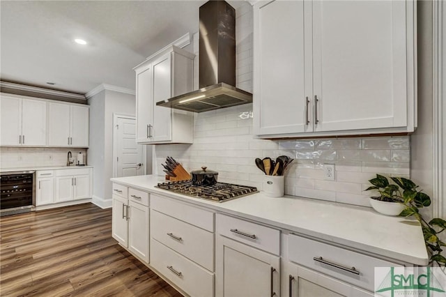 kitchen featuring wine cooler, crown molding, stainless steel gas stovetop, wood finished floors, and wall chimney exhaust hood