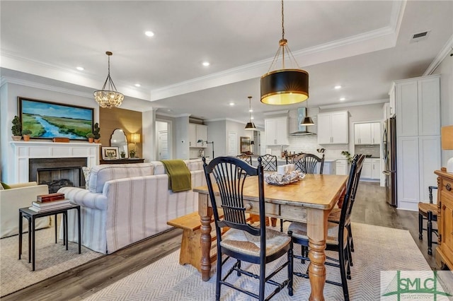 dining area with a tray ceiling, a fireplace, recessed lighting, visible vents, and wood finished floors