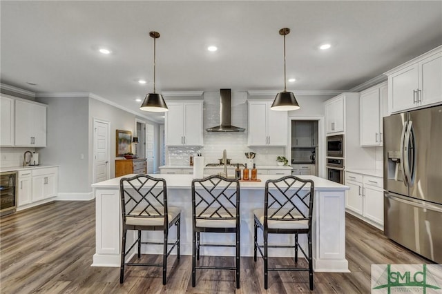 kitchen with stainless steel appliances, light countertops, white cabinetry, wall chimney range hood, and a kitchen bar