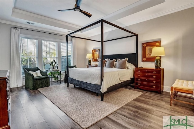 bedroom with crown molding, visible vents, a raised ceiling, and wood finished floors