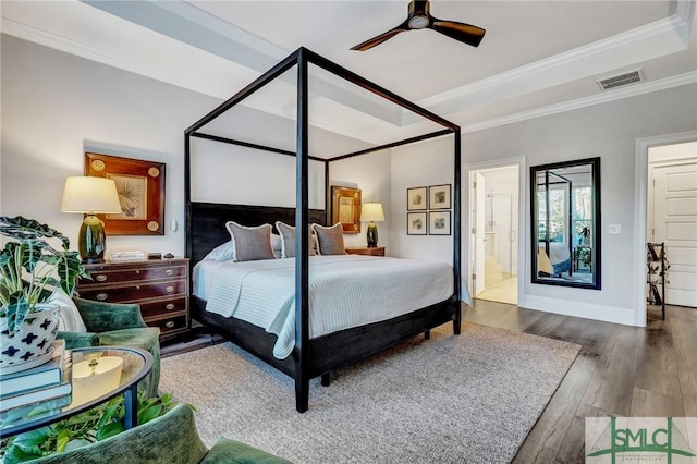 bedroom with connected bathroom, visible vents, ornamental molding, a tray ceiling, and wood-type flooring