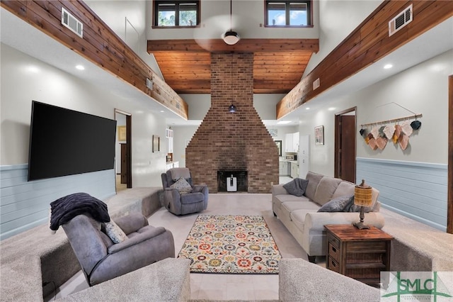 carpeted living area featuring high vaulted ceiling, a wainscoted wall, wood walls, a fireplace, and visible vents