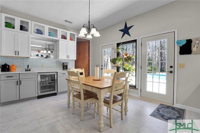 dining room featuring visible vents, an inviting chandelier, a textured ceiling, beverage cooler, and baseboards