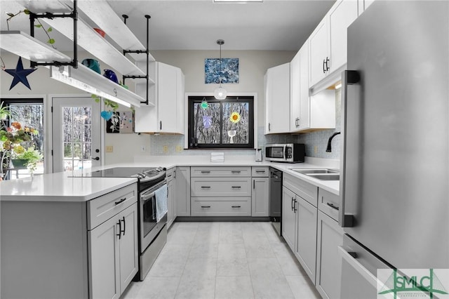 kitchen featuring a peninsula, a sink, light countertops, appliances with stainless steel finishes, and open shelves