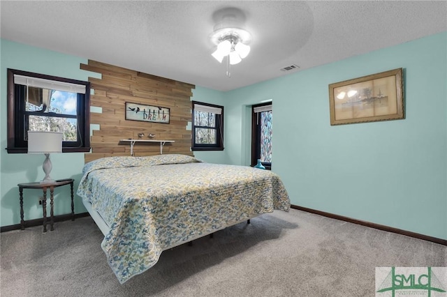 bedroom with visible vents, an accent wall, carpet flooring, a textured ceiling, and wood walls