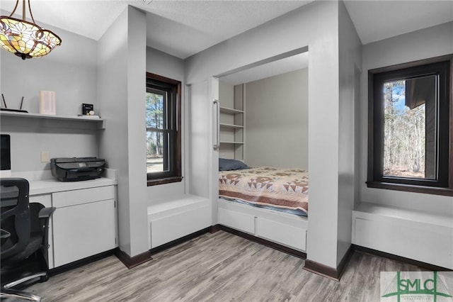 bedroom featuring light wood-type flooring, multiple windows, baseboards, and built in study area