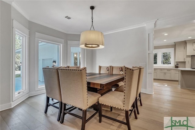 dining area featuring light wood-style floors, a wealth of natural light, visible vents, and crown molding