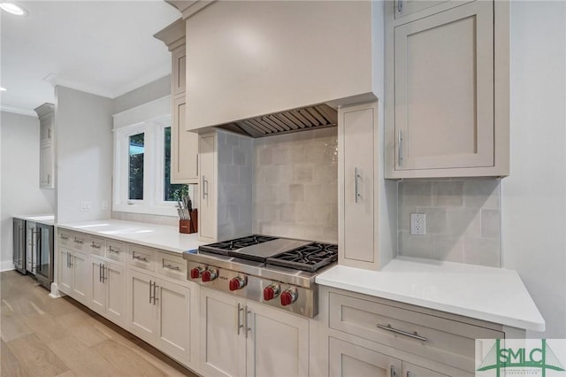 kitchen with light wood-type flooring, custom range hood, stainless steel gas cooktop, and backsplash