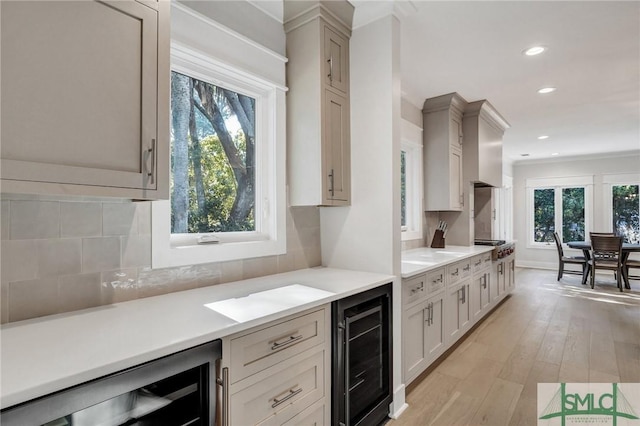 kitchen with light wood-style floors, a wealth of natural light, beverage cooler, and wall chimney exhaust hood