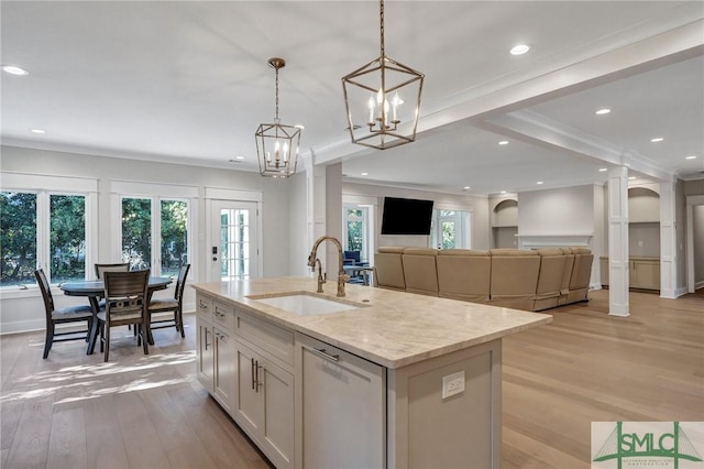 kitchen with light wood-style floors, a sink, dishwashing machine, and light stone countertops