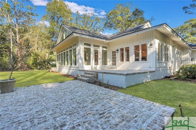 view of side of property with a yard, board and batten siding, a patio area, and a sunroom