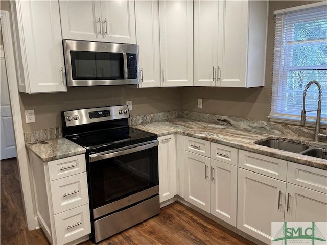 kitchen featuring dark wood-type flooring, light stone countertops, stainless steel appliances, white cabinetry, and a sink