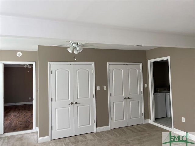 unfurnished bedroom featuring light carpet, washing machine and dryer, two closets, and baseboards