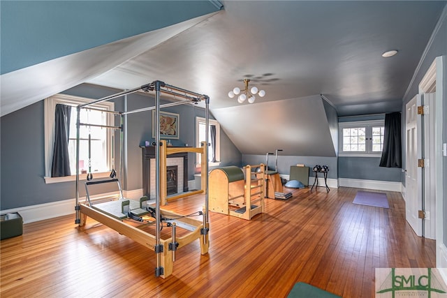 exercise area featuring lofted ceiling, a brick fireplace, hardwood / wood-style flooring, and baseboards