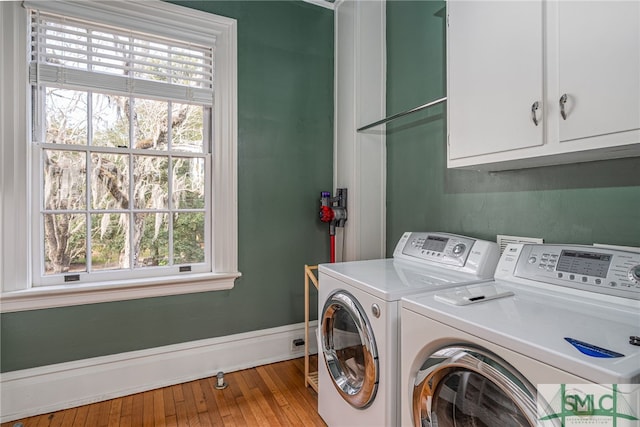 clothes washing area featuring cabinet space, washing machine and dryer, baseboards, and hardwood / wood-style flooring