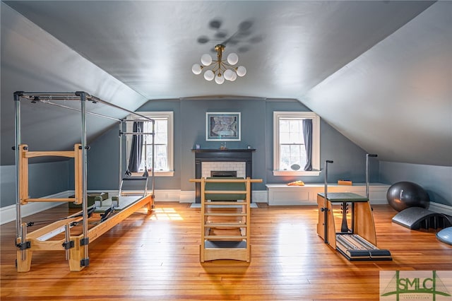 workout area with a brick fireplace, vaulted ceiling, baseboards, and hardwood / wood-style flooring