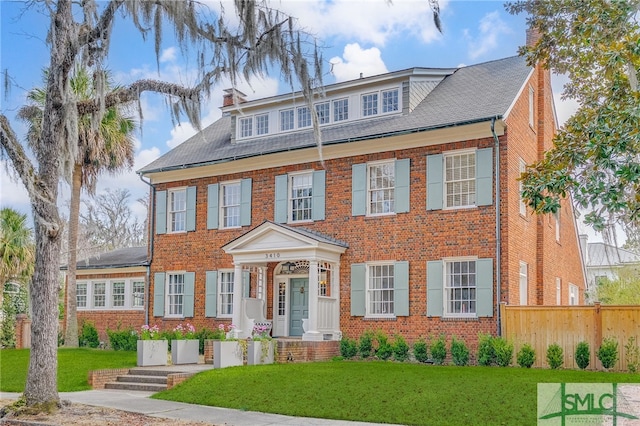 colonial home featuring brick siding, fence, a chimney, and a front lawn