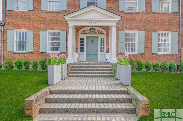 entrance to property with brick siding and a lawn