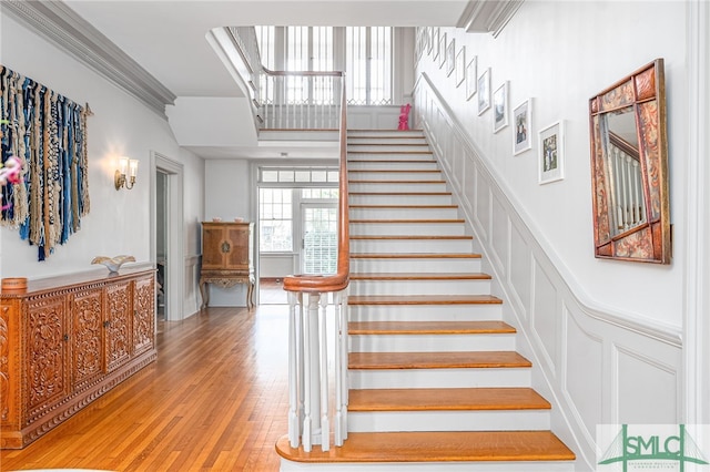 stairs with crown molding, wood finished floors, and a decorative wall