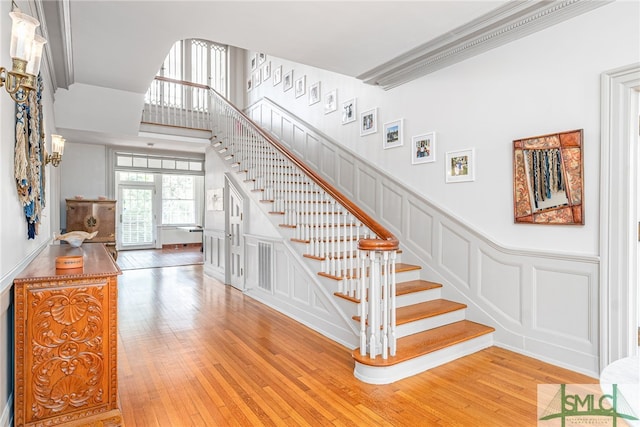 staircase with a towering ceiling, a wainscoted wall, a decorative wall, and hardwood / wood-style floors