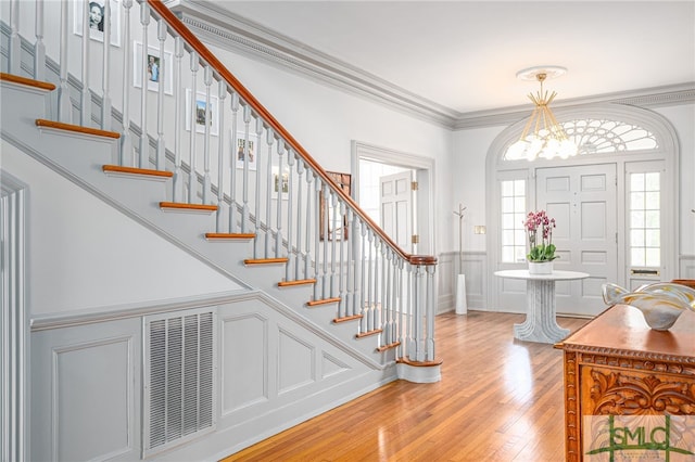 foyer with visible vents, hardwood / wood-style floors, stairs, crown molding, and a notable chandelier