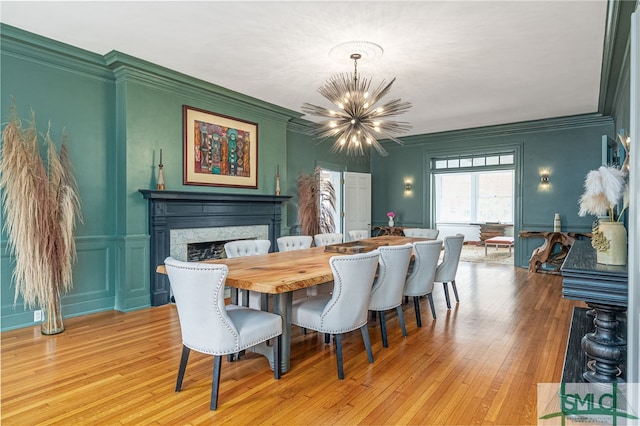 dining area with ornamental molding, a notable chandelier, a decorative wall, and light wood finished floors