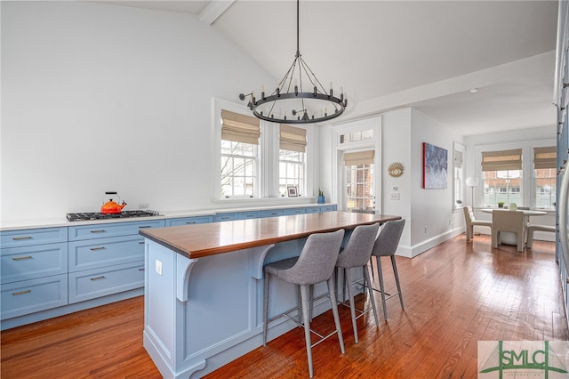 kitchen with a chandelier, wood-type flooring, blue cabinets, a kitchen bar, and stainless steel gas cooktop