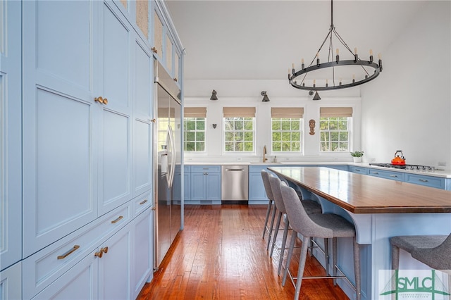 kitchen with a breakfast bar area, stainless steel appliances, wood-type flooring, a sink, and wood counters