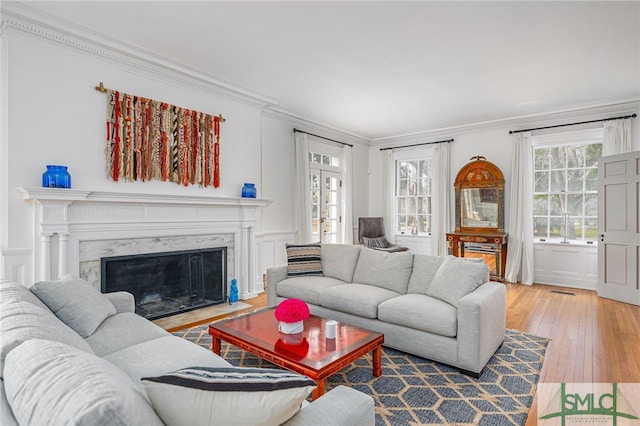 living area with ornamental molding, a premium fireplace, hardwood / wood-style flooring, and a decorative wall