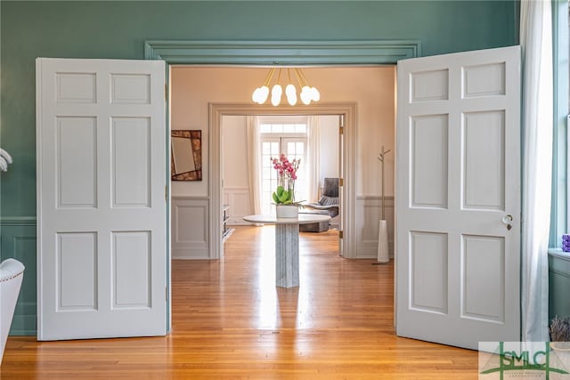 hallway featuring light wood-style flooring, a decorative wall, and wainscoting