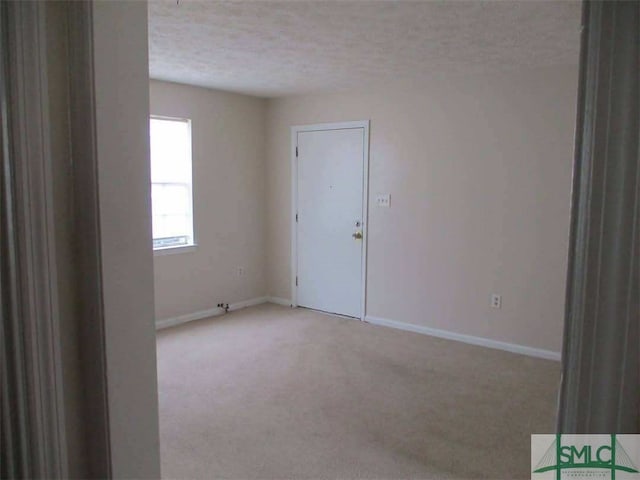 spare room with light carpet, baseboards, and a textured ceiling