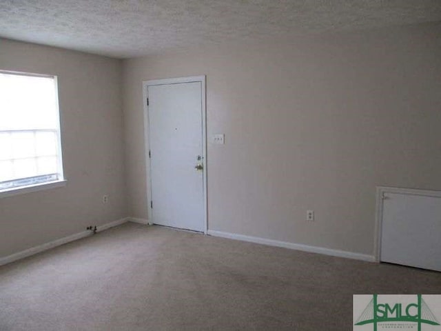 spare room featuring light colored carpet, a textured ceiling, and baseboards