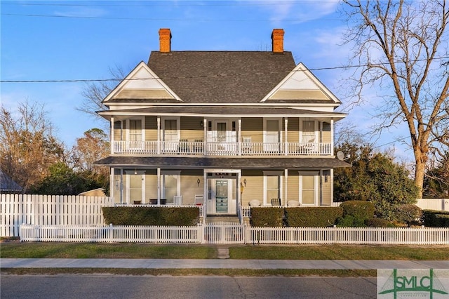 view of front of property featuring a balcony, covered porch, and a fenced front yard