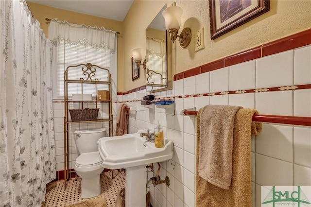 bathroom featuring a wainscoted wall, a shower with shower curtain, tile walls, and toilet