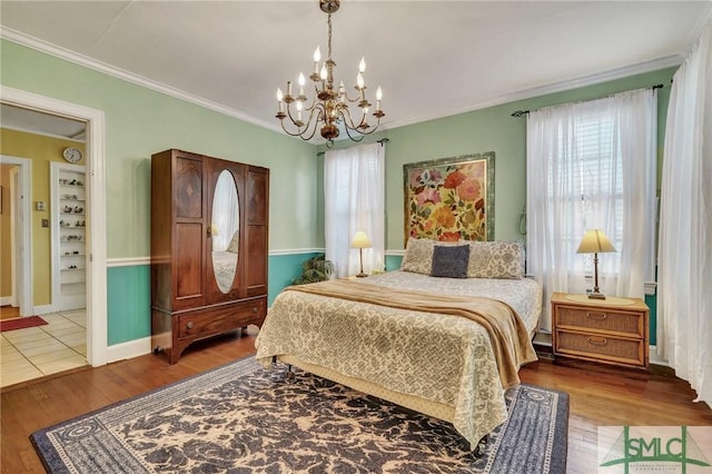 bedroom featuring baseboards, a notable chandelier, ornamental molding, and wood finished floors