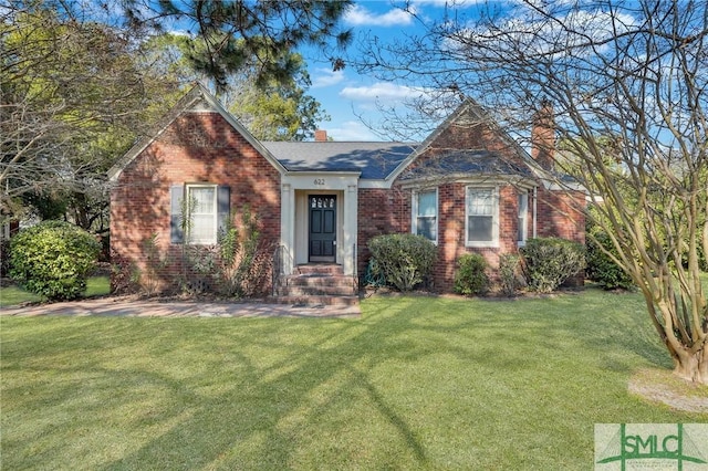 view of front facade with a front yard, a chimney, and brick siding